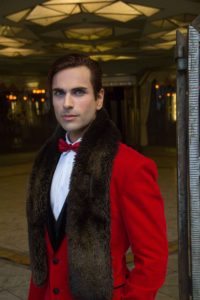A man in red jacket and fur collar standing on sidewalk.